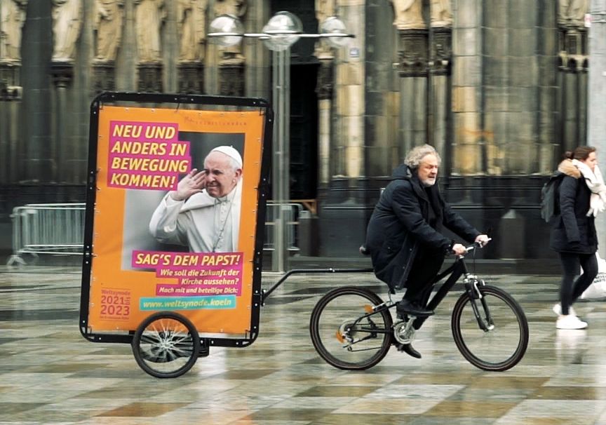 Weihbischof Rolf Steinhäuser fährt auf einem Plakat-Fahrrad 